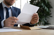 © fizkes - Crop close up of male employer sit at office desk hold paperwork correspondence analyzing report or statistics, Caucasian businessman read consider postal paper document or post letter at workplace