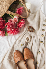 Wall Mural - Beauty fashion collage with women's clothes and accessory on white linen. Sun dress sarafan, leather shoes, pink peony flowers in straw bag. Flat lay, top view fashion blog lifestyle concept