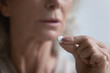 Close up of mature woman think of having drug or pill, feeling unhealthy sick at home, pensive doubtful senior female consider taking medicines, suffering from illness, elderly healthcare concept