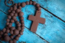 Brown Clay Crucifix And Beads On A Distressed Blue Tabletop