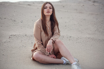 pretty yuong woman sitting on the sand in dress at desert background