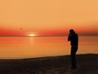 © Andrey - Back view of a silhouette of a man photographing the sun at sunset on the beach on holidays