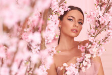 Closeup Fashion Spring Face Portrait Of Young Beautiful Caucasian Woman With Brunette Hair In Pony Tail And Perfect Makeup Looking Through Trees With Pink Flowers In Blossom
