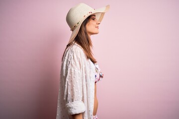 Wall Mural - Young beautiful woman on vacation wearing bikini and summer hat over pink background looking to side, relax profile pose with natural face with confident smile.