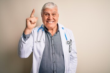 Wall Mural - Senior handsome hoary doctor man wearing coat and stethoscope over white background pointing finger up with successful idea. Exited and happy. Number one.