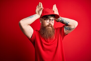 Wall Mural - Young handsome delivery man wearing glasses and red cap over isolated background Doing bunny ears gesture with hands palms looking cynical and skeptical. Easter rabbit concept.