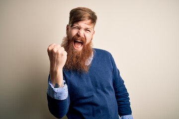 Canvas Print - Handsome Irish redhead business man with beard standing over isolated background angry and mad raising fist frustrated and furious while shouting with anger. Rage and aggressive concept.