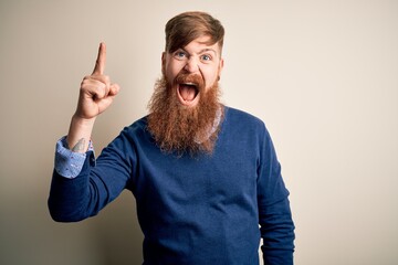 Wall Mural - Handsome Irish redhead business man with beard standing over isolated background pointing finger up with successful idea. Exited and happy. Number one.