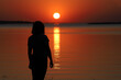 © Gerson - silhouette of woman admiring the sunset in golden, yellow and red tones, with the sun descending over the waters of a river.