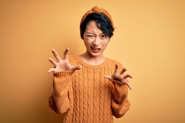 Poster - Young beautiful asian girl wearing casual sweater and diadem standing over yellow background smiling funny doing claw gesture as cat, aggressive and sexy expression