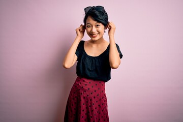 Poster - Young beautiful asian girl wearing casual dress standing over isolated pink background Smiling pulling ears with fingers, funny gesture. Audition problem