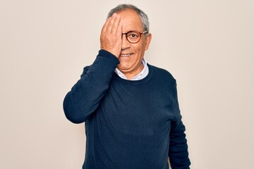 Canvas Print - Senior handsome grey-haired man wearing sweater and glasses over isolated white background covering one eye with hand, confident smile on face and surprise emotion.