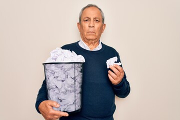 Wall Mural - Senior grey-haired man holding full paper bin with crumpled papers over white background with a confident expression on smart face thinking serious