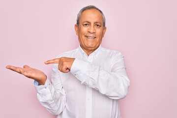 Sticker - Senior handsome grey-haired man wearing elegant shirt over isolated pink background amazed and smiling to the camera while presenting with hand and pointing with finger.