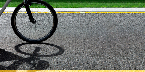 A bicycle wheel rides along an asphalt road with yellow markings and green grass on the sidelines on a sunny summer day with copy space, closeup 16:9.