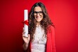 © Krakenimages.com - Young beautiful woman with curly hair holding university diploma degree over red background with a happy face standing and smiling with a confident smile showing teeth