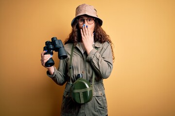 Sticker - Beautiful tourist woman on vacation wearing explorer hat and water canteen using binoculars cover mouth with hand shocked with shame for mistake, expression of fear, scared in silence, secret concept