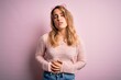 © Krakenimages.com - Young beautiful blonde woman wearing casual sweater and sunglasses over pink background with hand on stomach because indigestion, painful illness feeling unwell. Ache concept.
