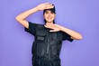 © Krakenimages.com - Young police woman wearing security bulletproof vest uniform over purple background Smiling cheerful playing peek a boo with hands showing face. Surprised and exited