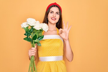 Sticker - Young beautiful pin up woman wearing 50s fashion vintage dress holding boquet of roses flowers doing ok sign with fingers, excellent symbol