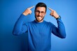 © Krakenimages.com - Young handsome man with beard wearing casual sweater and glasses over blue background smiling pointing to head with both hands finger, great idea or thought, good memory