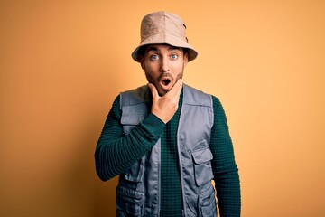 Canvas Print - Handsome tourist man with beard on vacation wearing explorer hat over yellow background Looking fascinated with disbelief, surprise and amazed expression with hands on chin