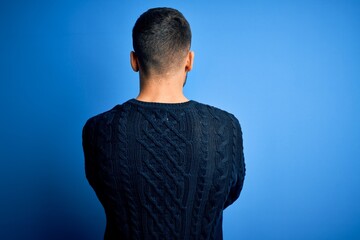 Young handsome man wearing casual sweater standing over isolated blue background standing backwards looking away with crossed arms