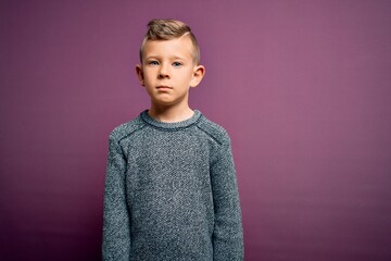 Wall Mural - Young little caucasian kid with blue eyes wearing winter sweater standing over purple background with serious expression on face. Simple and natural looking at the camera.