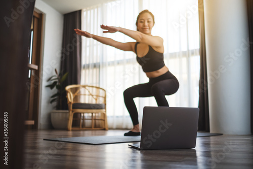 Fotomural A beautiful young asian woman doing squats while watching online workout tutoria
