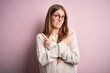 © Krakenimages.com - Young beautiful redhead woman wearing casual sweater and glasses over pink background Pointing to both sides with fingers, different direction disagree
