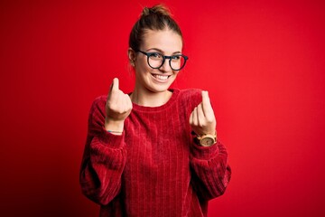 Wall Mural - Young beautiful redhead woman wearing casual sweater over isolated red background doing money gesture with hands, asking for salary payment, millionaire business