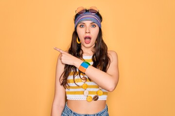 Wall Mural - Young beautiful hippie woman with blue eyes wearing accesories and sunnglasses Surprised pointing with finger to the side, open mouth amazed expression.