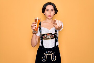 Wall Mural - Young beautiful german woman with blue eyes wearing octoberfest dress drinking glass of beer pointing with finger to the camera and to you, hand sign, positive and confident gesture from the front