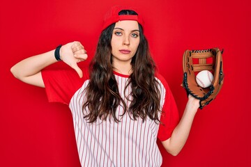 Wall Mural - Young beautiful sportswoman with blue eyes playing baseball using glove and ball with angry face, negative sign showing dislike with thumbs down, rejection concept