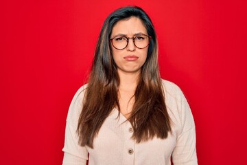 Poster - Young hispanic smart woman wearing glasses standing over red isolated background depressed and worry for distress, crying angry and afraid. Sad expression.