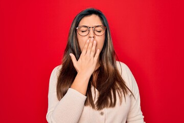 Sticker - Young hispanic smart woman wearing glasses standing over red isolated background bored yawning tired covering mouth with hand. Restless and sleepiness.