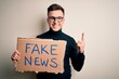 © Krakenimages.com - Young handsome caucasian man holding protest carboard for desinformation and fake news surprised with an idea or question pointing finger with happy face, number one