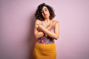 Wall Mural - Young beautiful arab woman on vacation wearing swimsuit and sunglasses over pink background Pointing to both sides with fingers, different direction disagree