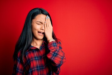 Wall Mural - Young beautiful chinese woman wearing casual shirt over isolated red background Yawning tired covering half face, eye and mouth with hand. Face hurts in pain.