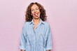 © Krakenimages.com - Middle age beautiful woman wearing casual denim shirt standing over pink background sticking tongue out happy with funny expression. Emotion concept.