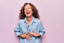 Middle Age Beautiful Woman Wearing Casual Denim Shirt Standing Over Pink Background Smiling And Laughing Hard Out Loud Because Funny Crazy Joke With Hands On Body.