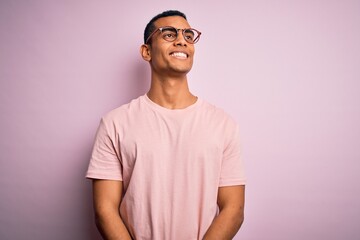 Poster - Handsome african american man wearing casual t-shirt and glasses over pink background looking away to side with smile on face, natural expression. Laughing confident.