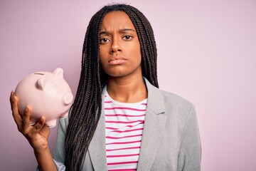 Young african american business woman saving money on piggy bank over isolated background with a confident expression on smart face thinking serious