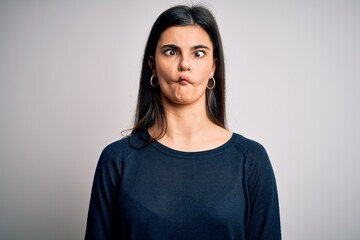 Young beautiful brunette woman wearing casual sweater standing over white background making fish face with lips, crazy and comical gesture. Funny expression.