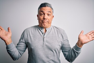 Poster - Middle age handsome grey-haired man wearing casual t-shirt over white background clueless and confused expression with arms and hands raised. Doubt concept.