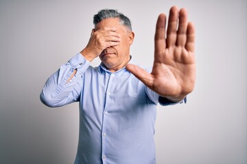 Poster - Middle age handsome grey-haired business man wearing elegant shirt over white background covering eyes with hands and doing stop gesture with sad and fear expression. Embarrassed and negative concept.