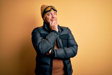 Poster - Middle age handsome grey-haired skier man on vacation wearing ski goggles looking confident at the camera with smile with crossed arms and hand raised on chin. Thinking positive.