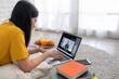 © weedezign - Asian female student video conference with teacher and friends using e-learing app on laptop computer at home.woman lying down on carpet.new normal learning online lifestyle