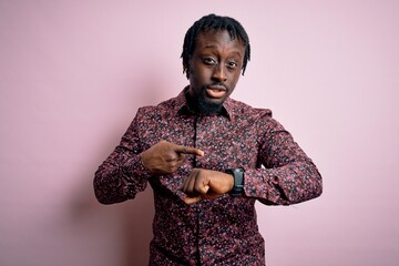 Poster - Young handsome african american man wearing casual shirt standing over pink background In hurry pointing to watch time, impatience, upset and angry for deadline delay