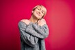 © Krakenimages.com - Young blonde woman with modern short hair wearing casual sweater over pink background Hugging oneself happy and positive, smiling confident. Self love and self care